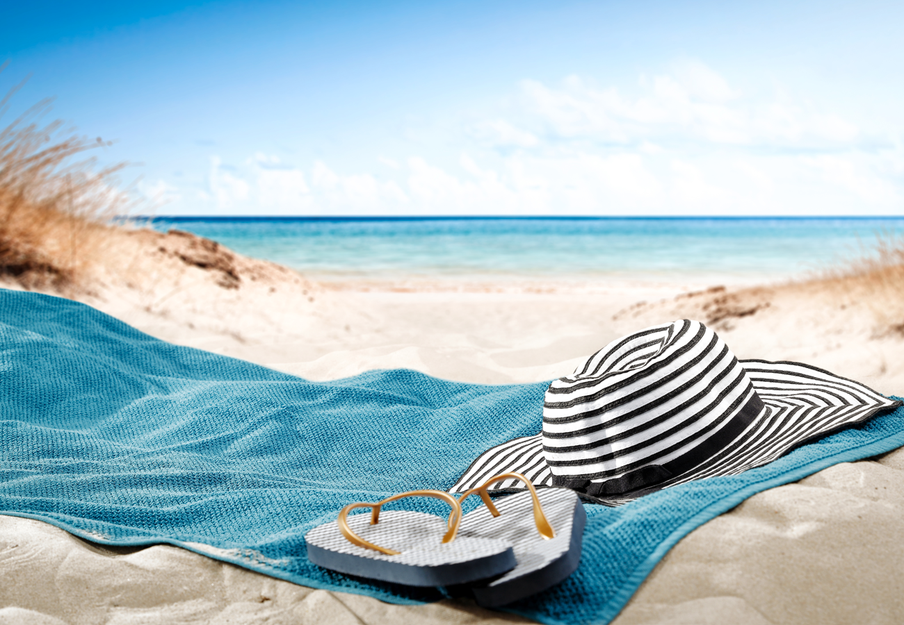 Hat and flip-flops on blue towel on sandy beach
