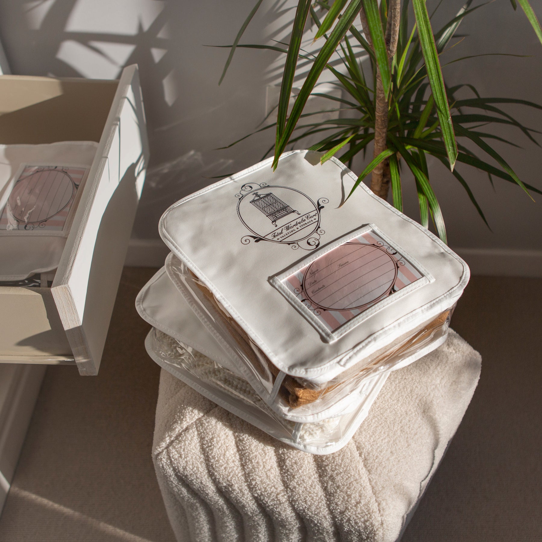 2 Knitwear & T-Shirt Storage bags stacked on top of stool beside indoor plant