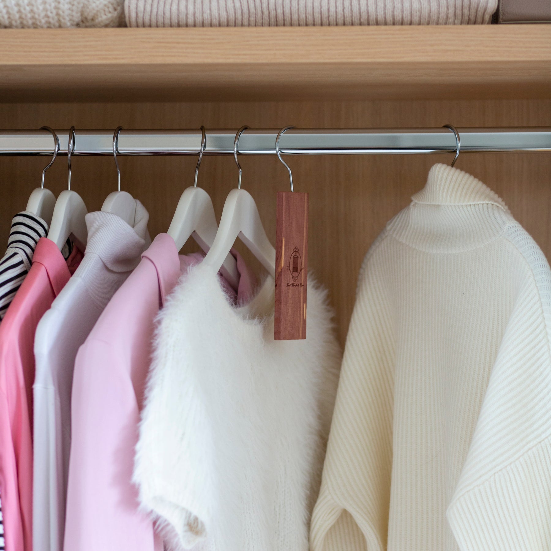 Cedarwood hanging block hanging from railing of wardrobe surrounded by light garments