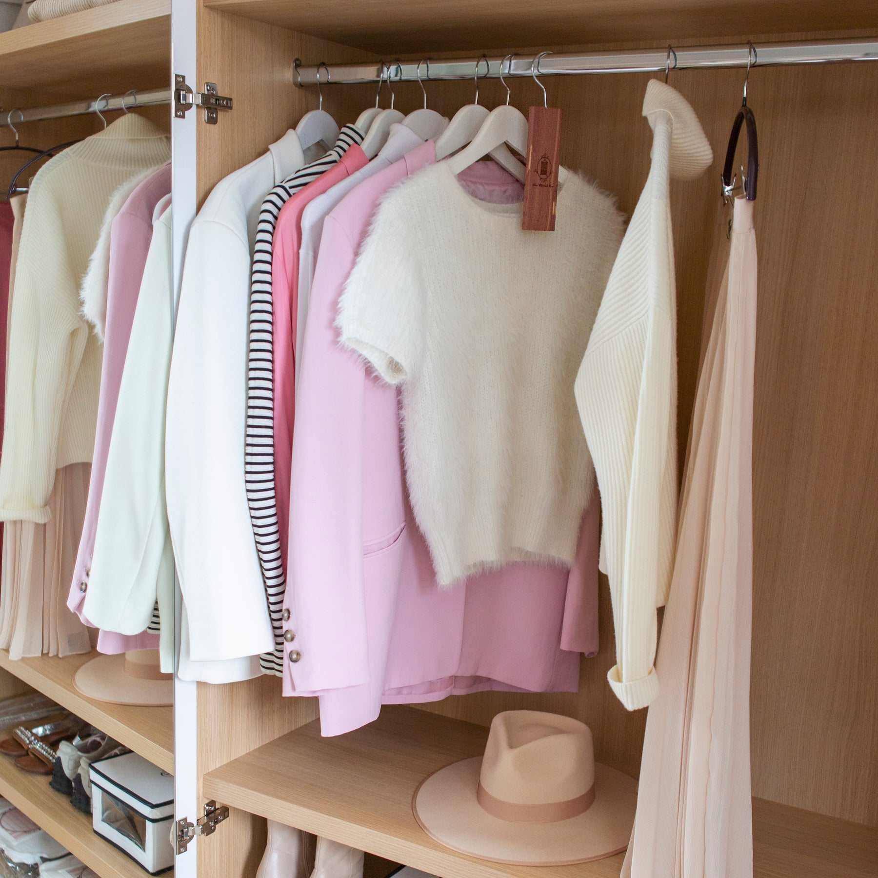 View of open wardrobe with light coloured clothing hanging on rail beside cedarwood hanging block