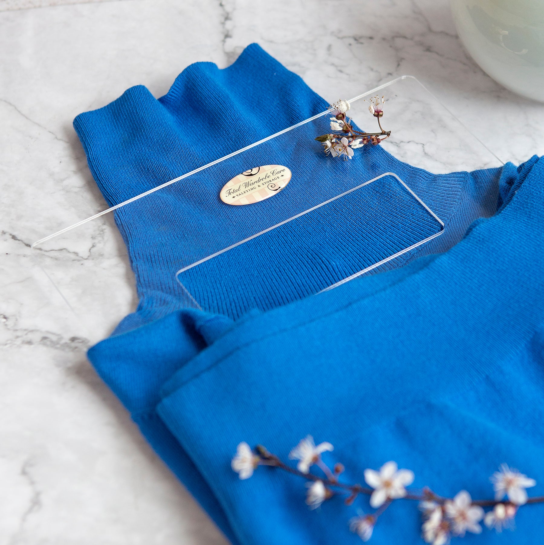 Blue turtle neck folded on folding palette on white marble surface with small white flowers present