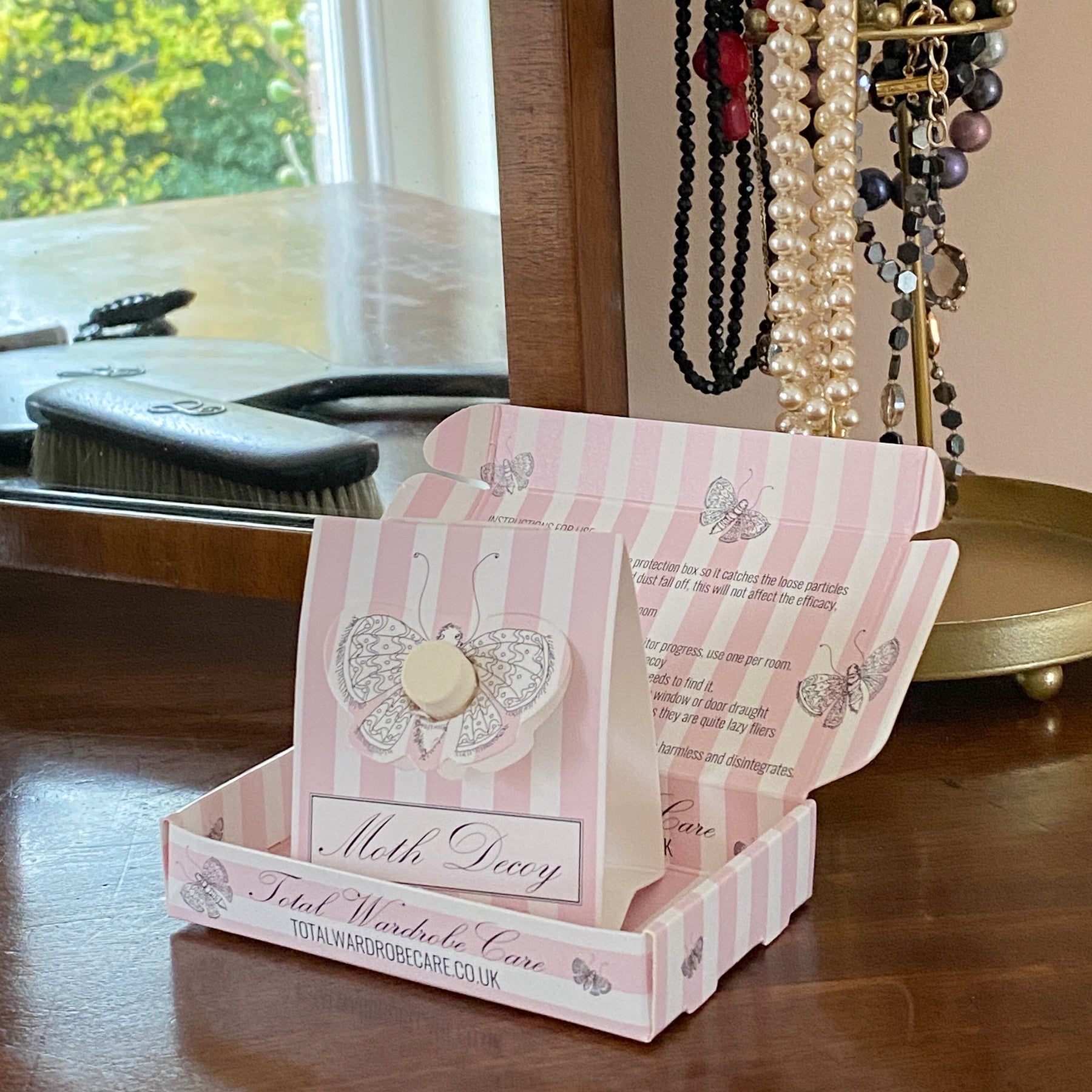 Moth Decoy stood inside pink and white packaging on dark wood table beside jewellery tree