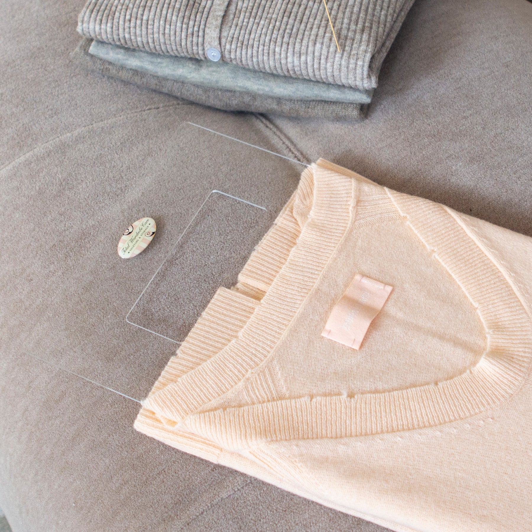 Peach cashmere jumper being folded using the Total Wardrobe Care folding palette beside stack of folded clothes