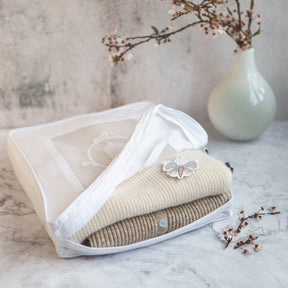 Open knitwear bag with 2 cashmere jumpers folded inside with vase containing cherry blossoms inside