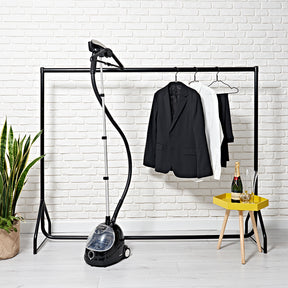 Fridja clothes steamer F-1000 stood beside rack with hanging suit with white brick wall to reverse and bottle of champagne to small yellow table