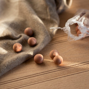 6 cedarwood balls on cashmere jumper with open bag to background all resting on wooden surface