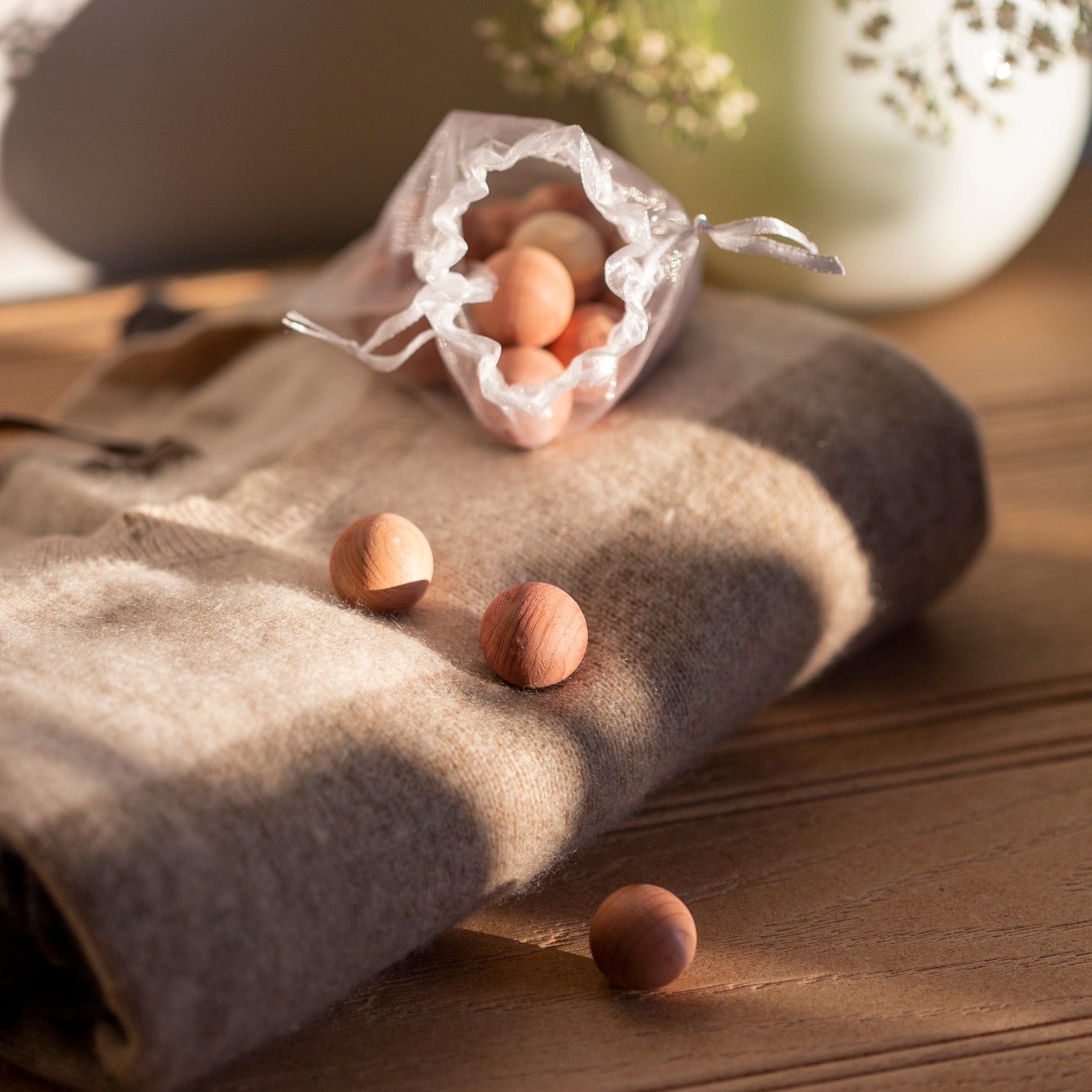 Open bag of cedarwood anti-moth balls and 3 loose balls on grey cashmere jumper