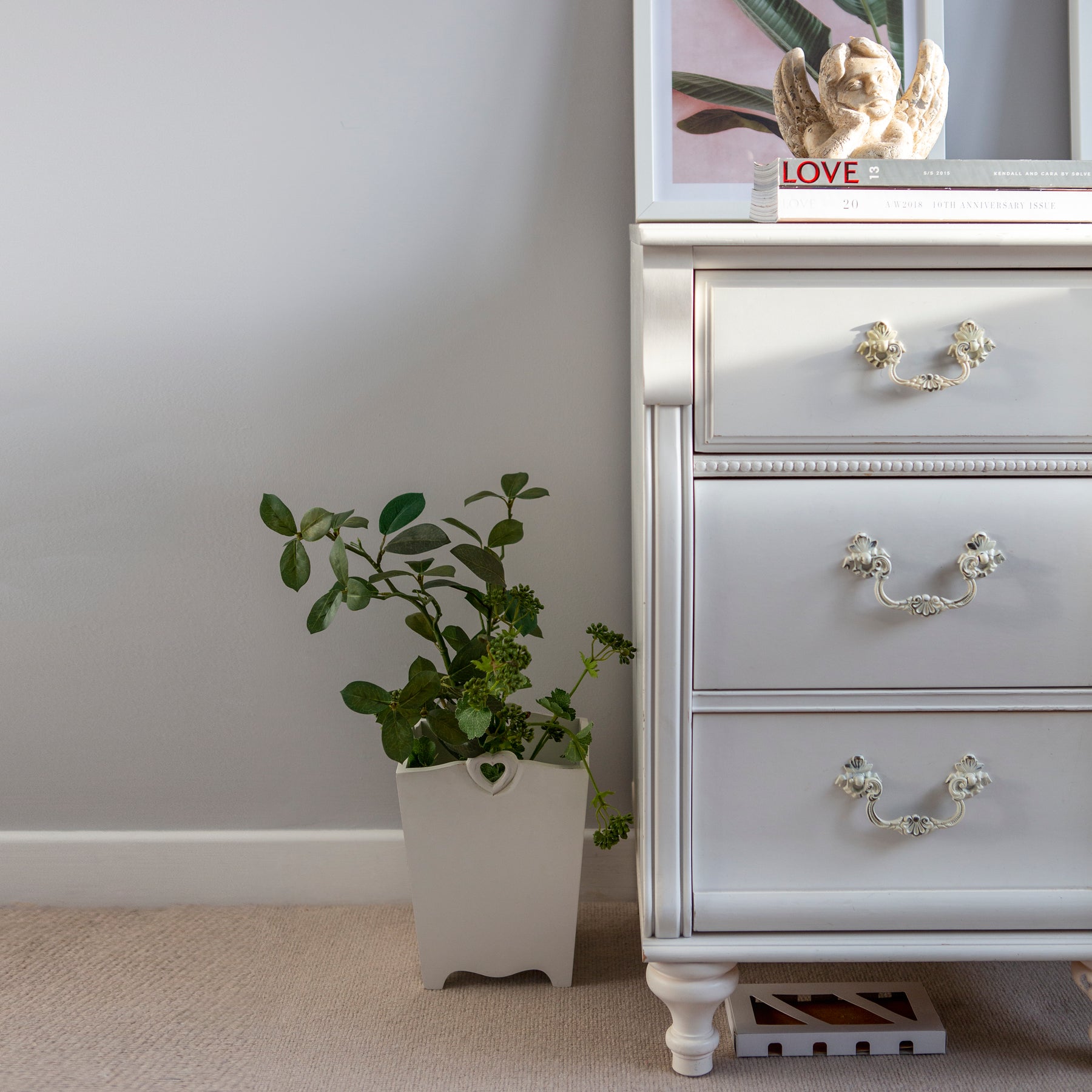 Chest of drawers with gorgeous white handles stood above moth box with plant to side