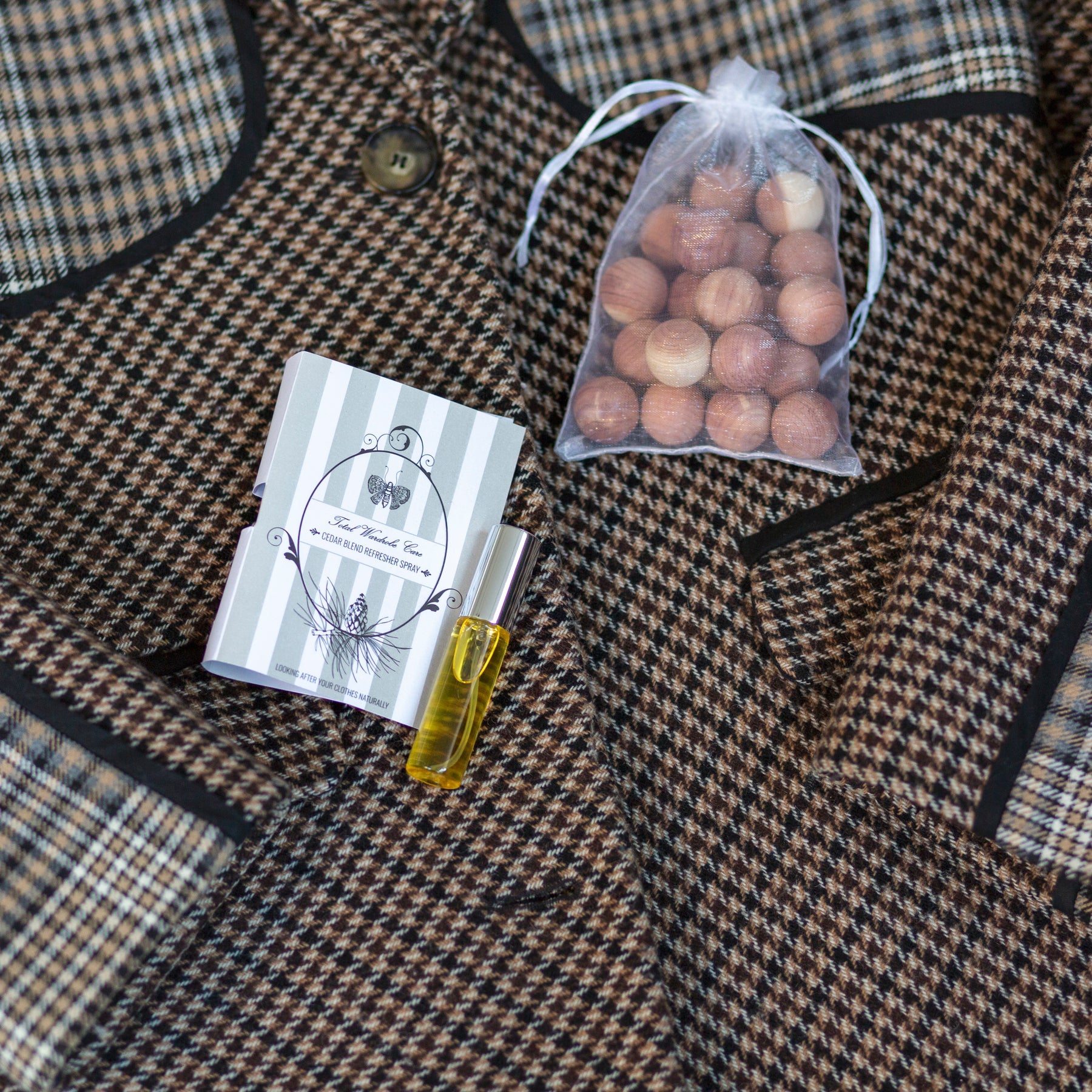 Closed organza bag filled with cedarwood balls beside refresher spray on top of tweed jacket
