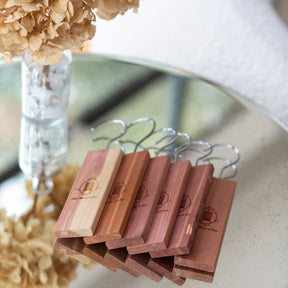 A row of cedarwood hanging blocks lined on a mirrored circular table with vase of dried flowers to the side