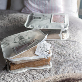 2 Total Wardrobe Care Wool Storage bags on a bed with one of them open showing a woollen garment and moth preventing drawer sachet