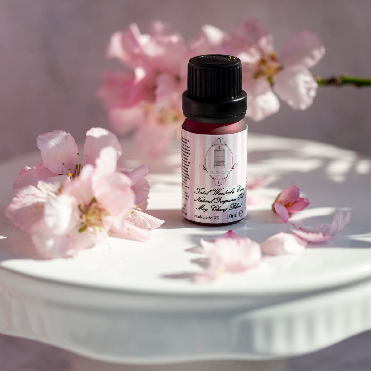 Small twist cap pink bottle of May Chang blend essential oil surrounded by pink flowers