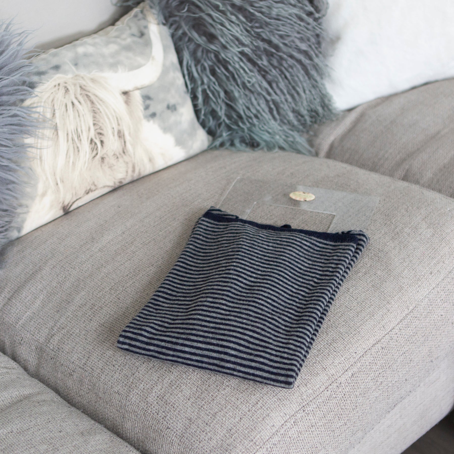 Striped folded garment on folding palette resting on sofa with highland cow cushion to reverse