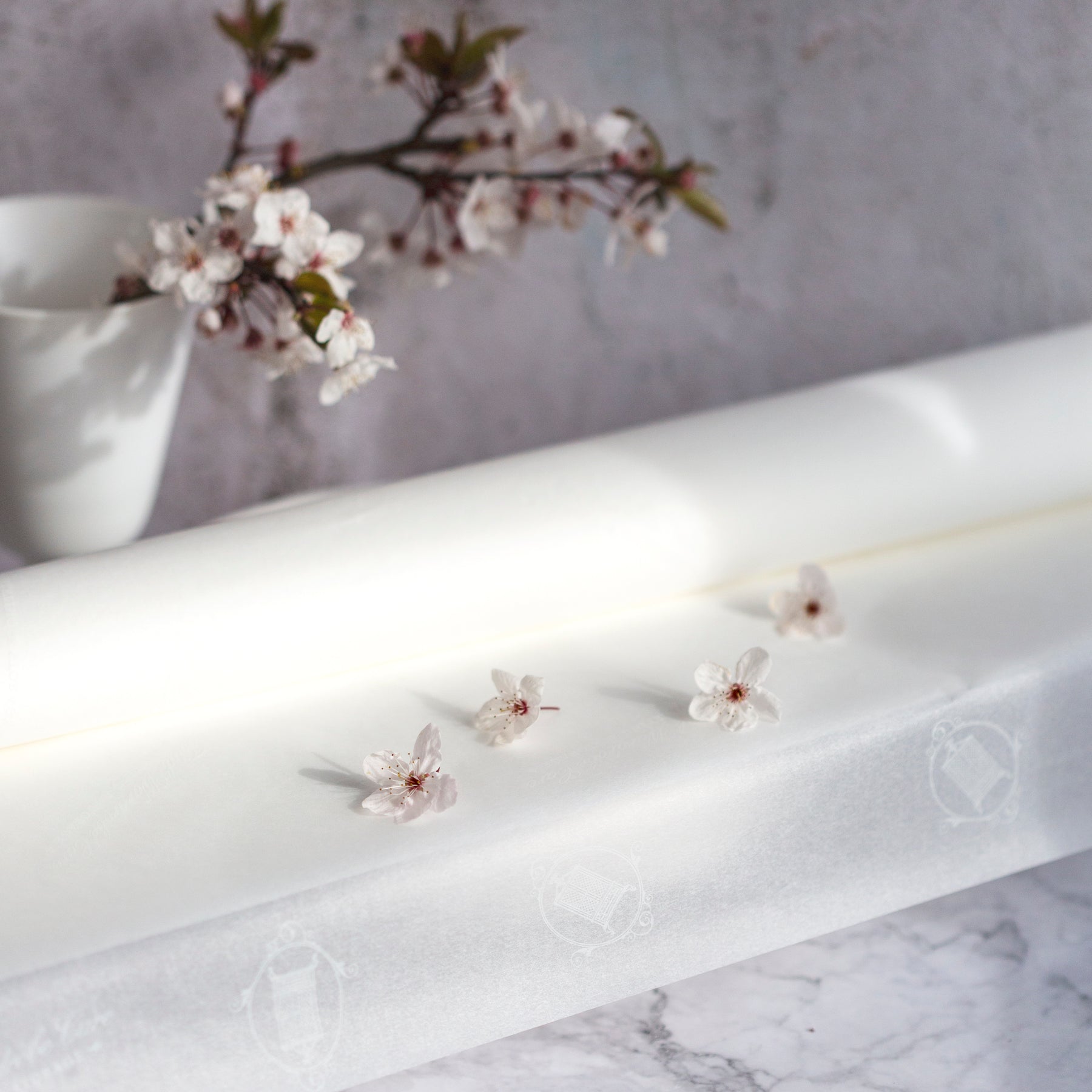 Open roll of acid-free tissue paper with 4 cherry blossoms on top and a twig of cherry blossom to reverse