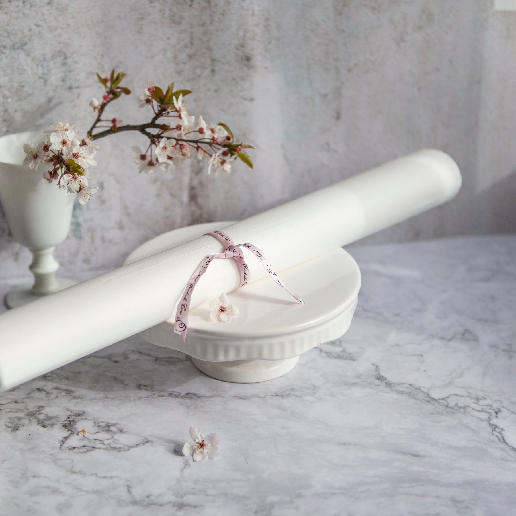 Roll of acid-free tissue paper sealed with pink ribbon on small ceramic podium on marble background