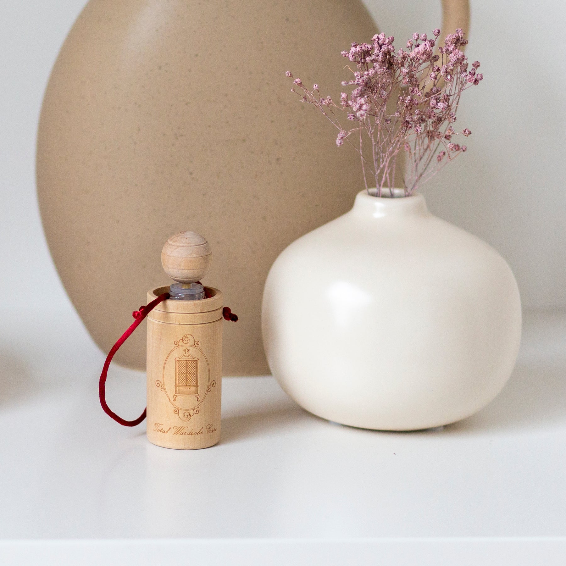 Wooden diffuser cup beside smooth white vase with small pink flowers inside