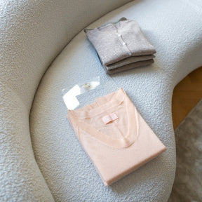 Peach jumper being folded on folding palette by Total Wardrobe Care on brushed fabric sofa