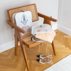 2 Wool Garment bags on a wooden chair with the Total Wardrobe Care logo visible on the front of both bags. A pair of ladies shoes are under the chair