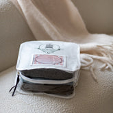 A white Total Wardrobe Care Knitwear bag with the zip undone, showing a grey wool garment inside. The bag is on a cream sofa with a cream blanket in the background