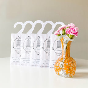 Row of May Chang Hanging Sachets beside abstract orange and white glass vase