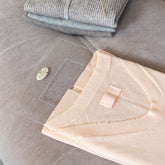 Peach cashmere jumper being folded using the Total Wardrobe Care folding palette beside stack of folded clothes